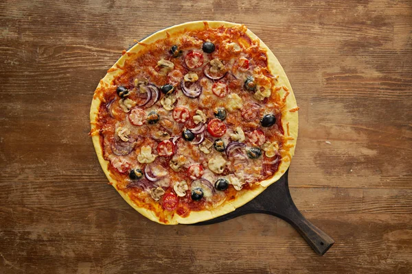 Top view of delicious pizza with cherry tomatoes, olives and parmesan on cutting board on wooden background — Stock Photo