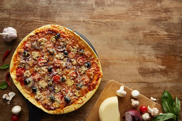 Vista superior de pizza y verduras sobre fondo de madera - foto de stock