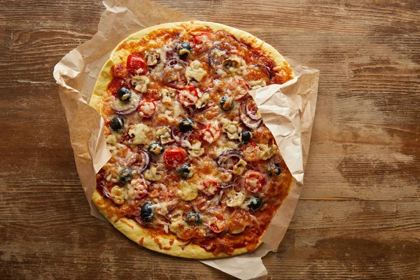 Vue du dessus de délicieuse pizza sur papier parchemin sur fond en bois — Photo de stock