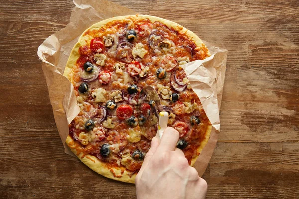 Cropped view of man cutting with knife pizza on wooden background — Stock Photo