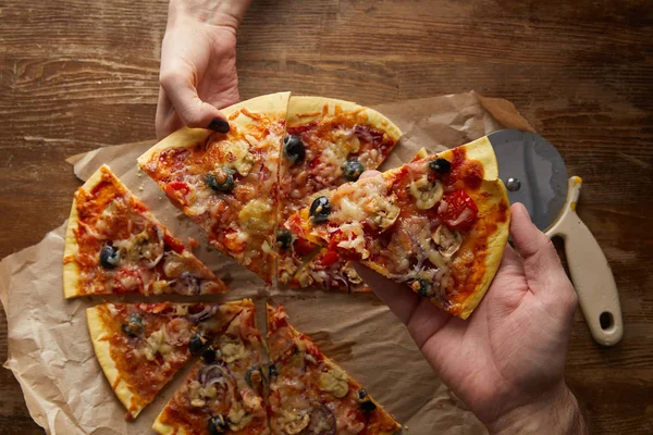 Vista cortada de casal comendo pizza juntos no fundo de madeira — Fotografia de Stock