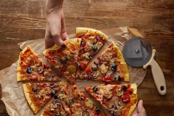 Vista recortada de la pareja comiendo pizza sobre fondo de madera - foto de stock