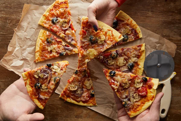 Vista cortada de amigos comendo pizza no fundo de madeira — Fotografia de Stock