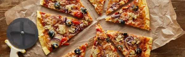 Vista dall'alto della deliziosa pizza italiana tagliata con olive su carta da forno vicino al coltello della pizza su sfondo di legno, colpo panoramico — Foto stock