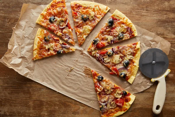 Vista dall'alto della deliziosa pizza italiana tagliata con olive su carta da forno vicino al coltello della pizza su sfondo di legno — Foto stock