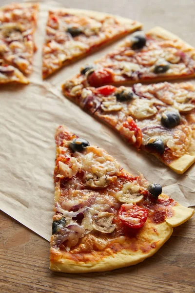Резать вкусную итальянскую пиццу с оливками на бумаге для выпечки на деревянном фоне — стоковое фото