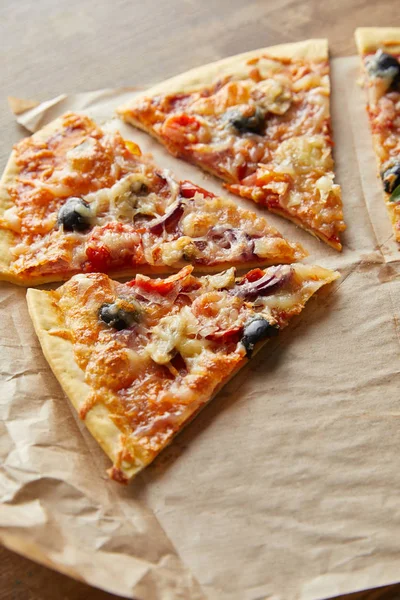 Couper de délicieuses pizzas italiennes aux olives sur papier cuisson sur fond bois — Photo de stock