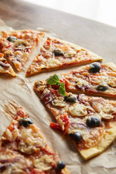 Couper de délicieuses pizzas italiennes aux olives sur papier cuisson sur table en bois — Photo de stock