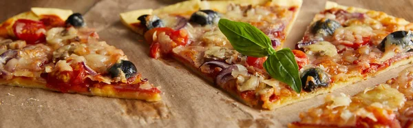 Cortar deliciosa pizza italiana com azeitonas e manjericão sobre papel manteiga na mesa de madeira, tiro panorâmico — Fotografia de Stock