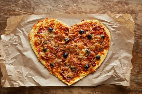 Top view of delicious italian pizza in heart shape on baking paper on wooden table — Stock Photo