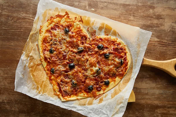 Vista superior da deliciosa pizza italiana em forma de coração no papel manteiga na mesa de madeira — Fotografia de Stock