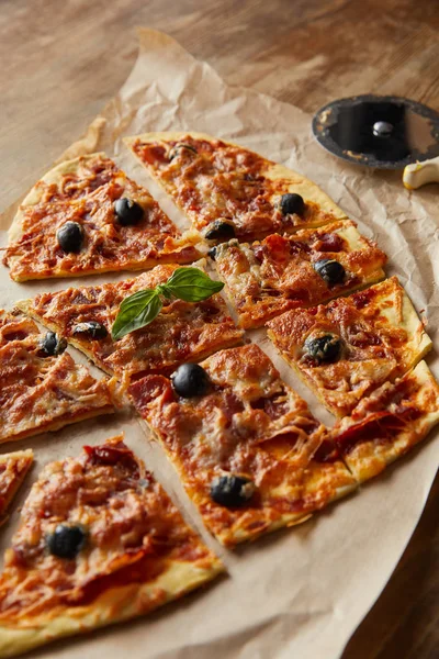 Close up view of delicious italian pizza in heart shape cut into pieces on baking paper near pizza knife on wooden table — Stock Photo