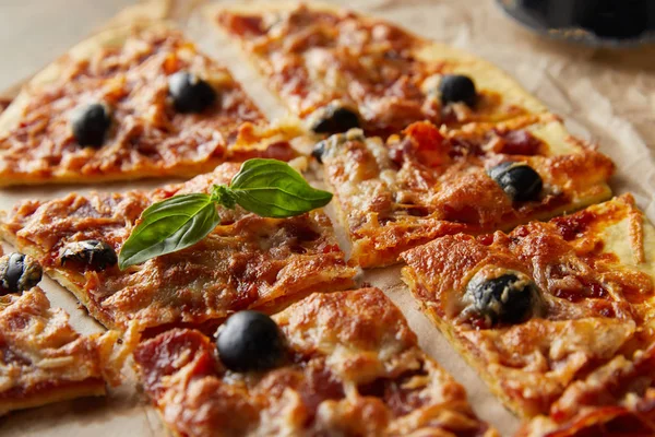 Vue rapprochée de délicieuses pizzas italiennes au basilic coupé en morceaux sur papier cuisson — Photo de stock