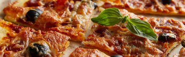 Vue rapprochée de délicieuses pizzas italiennes au basilic coupé en morceaux sur papier cuisson, plan panoramique — Photo de stock