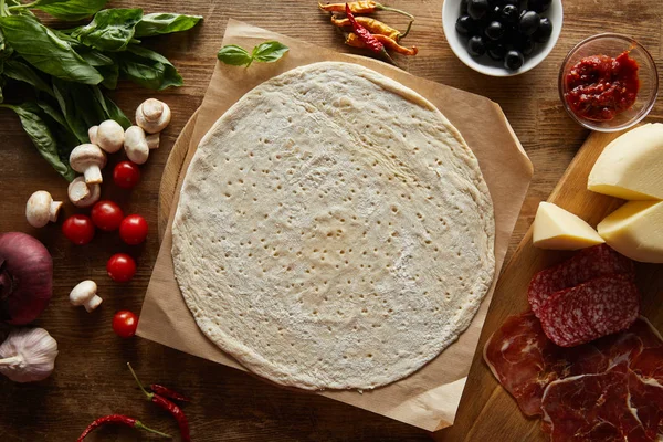 Vista superior de masa cruda con ingredientes para pizza en mesa de madera - foto de stock
