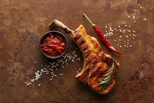 Top view of ribeye steak with tomato sauce, rosemary and chili pepper on stone surface — Stock Photo