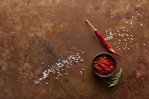 Вид зверху на томатний соус у мисці з перцем чилі, розмарином та сіллю на поверхні каменю — стокове фото