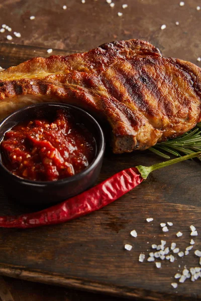 Selective focus of grilled steak with tomato sauce and chili pepper on cutting board on stone background — Stock Photo