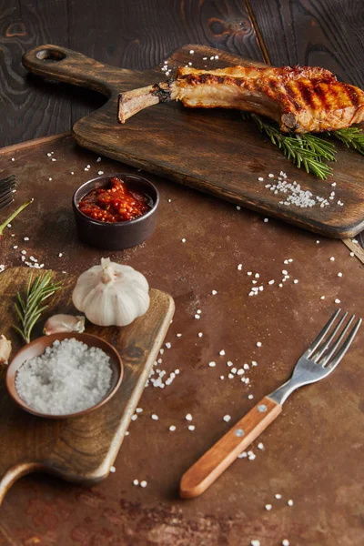 Enfoque selectivo de delicioso filete de ribeye en la tabla de cortar con ajo y salsa de tomate en tablero de piedra en la superficie de madera - foto de stock