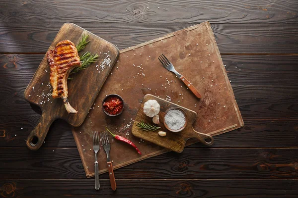 Вид сверху на вкусный стейк на разделочной доске с соусом чили, эмари и солью на каменной доске на деревянном фоне — стоковое фото
