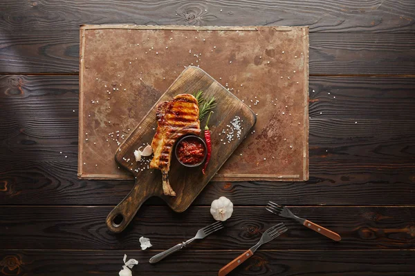 Top view of grilled ribeye steak with garlic, rosemary and chili sauce on stone board on wooden background — Stock Photo