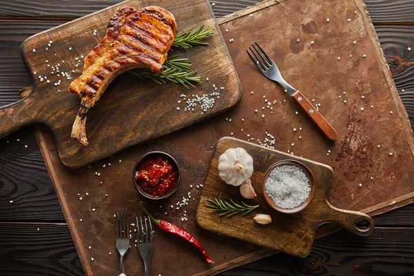 Top view of ribeye steak on cutting board with chili sauce and garlic on stone board on wooden background — Stock Photo