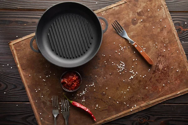 Top view of frying pan with chili sauce and salt on stone board on wooden background — Stock Photo
