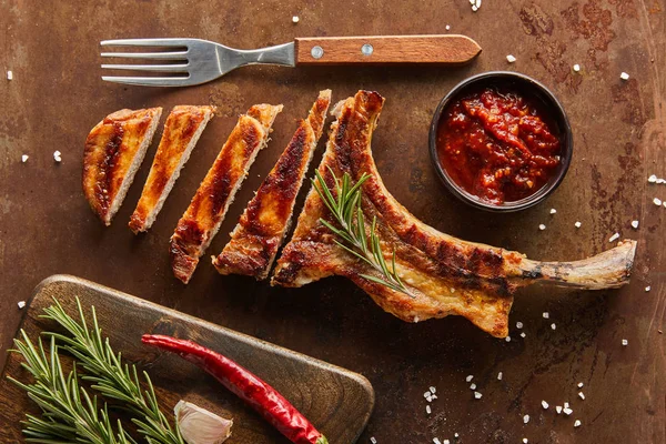 Top view of sliced ribeye steak with chili sauce, rosemary and garlic on stone surface — Stock Photo