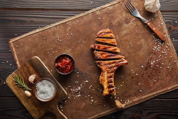 Top view of delicious ribeye steak with tomato sauce, garlic and salt on stone board on wooden surface — Stock Photo