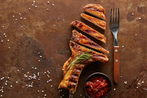 Top view of tasty ribeye steak with rosemary, tomato sauce and fork on textured stone surface — Stock Photo