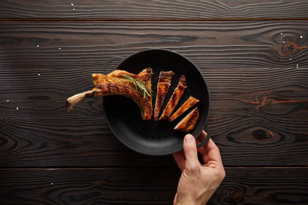 Top view of man holding frying pan with delicious ribeye steak on wooden background — Stock Photo