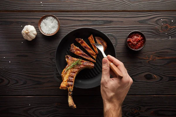 Vista superior del hombre sosteniendo tenedor con rebanada de filete por salsa de tomate, sal y ajo sobre fondo de madera — Stock Photo