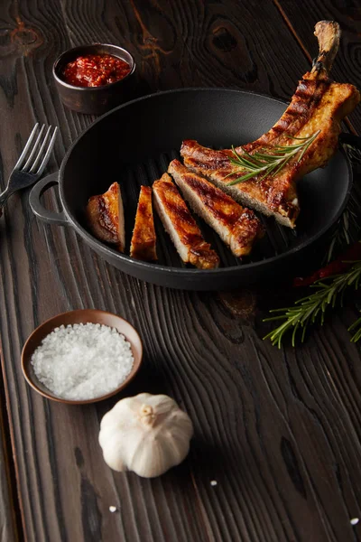 Selektiver Schwerpunkt des Ribeye-Steaks in der Pfanne mit Tomatensauce, Knoblauch und Salz auf hölzernem Hintergrund — Stockfoto