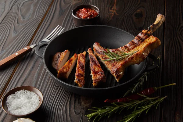 Grilled ribeye steak in frying pan with rosemary, tomato sauce and fork on wooden background — Stock Photo