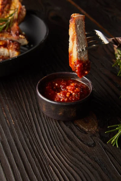 Slice of delicious steak on fork by tomato sauce and rosemary on wooden surface — Stock Photo