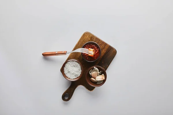 Top view of slice of steak on fork by tomato sauce, garlic and salt on cutting board on white background — Stock Photo