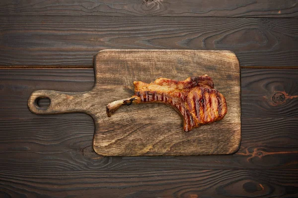 Top view of grilled ribeye steak on cutting board on wooden surface — Stock Photo