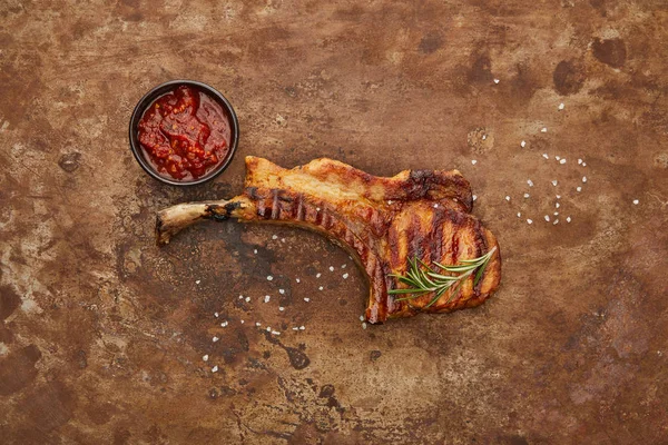 Blick von oben auf köstliches Ribeye-Steak mit Tomatensauce und Rosmarin auf Steinoberfläche — Stockfoto