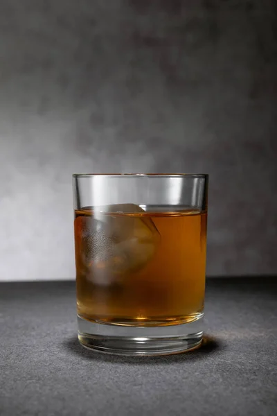 Cubo de hielo congelado en vaso de whisky sobre gris - foto de stock