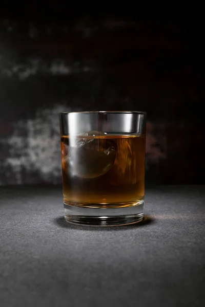Frozen ice cube in glass of whiskey on black with smoke — Stock Photo
