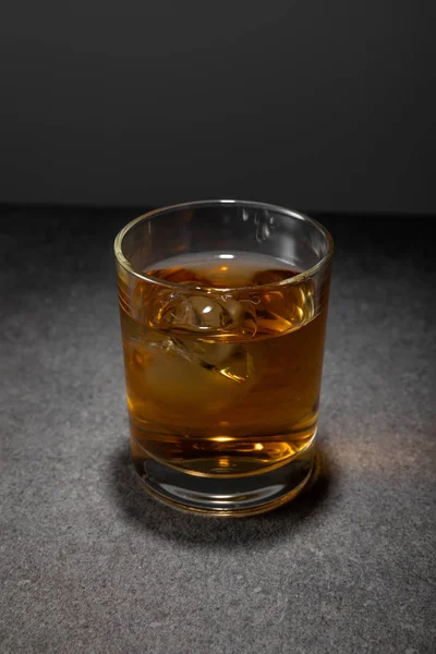 Frozen ice cubes in glass of whiskey on grey surface — Stock Photo