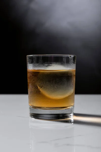 Ice cube in glass of whiskey on black with smoke — Stock Photo