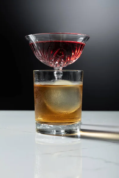 Foco selectivo de cubo de hielo en vaso de whisky cerca de vino tinto en negro - foto de stock