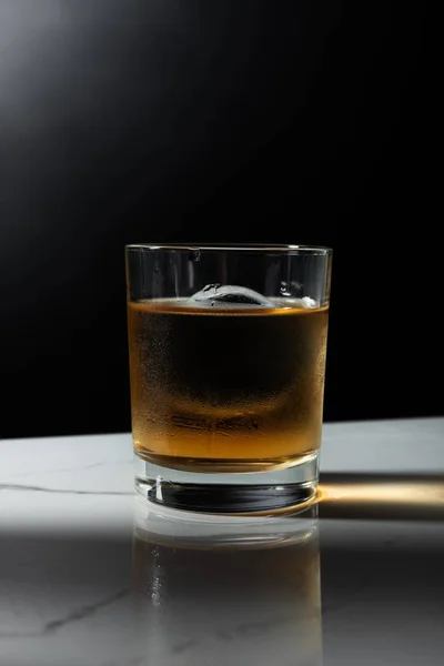 Ice cube in glass of strong whiskey isolated on black — Stock Photo