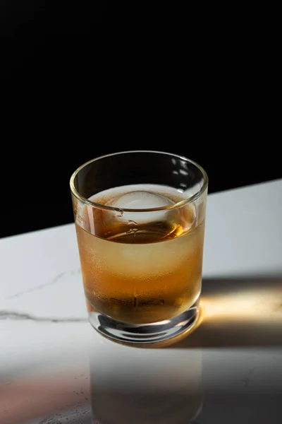 Ice cube in glass of whiskey isolated on black — Stock Photo
