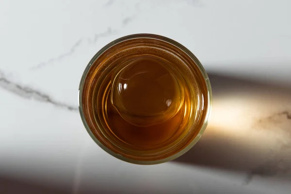 Top view of ice cube in glass of whiskey on white marble surface — Stock Photo