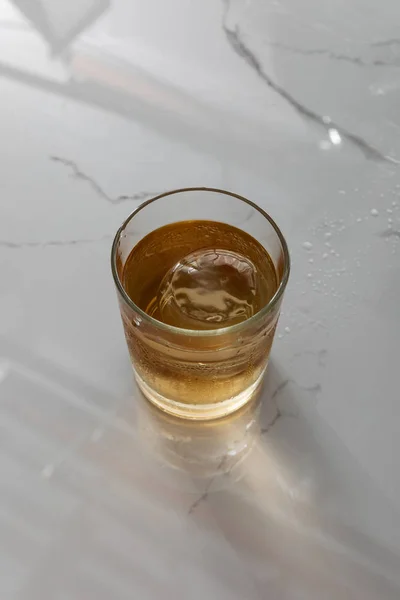 Вид сверху на стекло с виски и кубиком льда на поверхности белого мрамора — стоковое фото