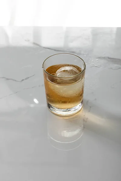 Glass of whiskey with ice cube on white marble surface — Stock Photo
