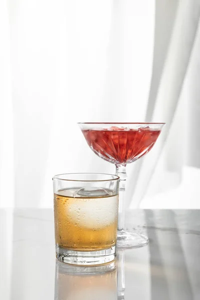 Склянка міцного віскі біля червоного коктейлю на білому — стокове фото