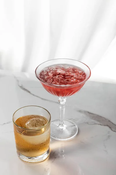 Glass of strong brandy near red cocktail with ice cubes on white — Stock Photo